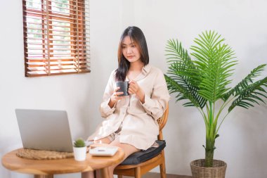 Oturma odasında faaliyet kavramı, genç Asyalı bir kadının kahve içip dizüstü bilgisayardan film izlemesi..