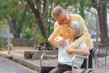 Yaşlı adam tekerlekli sandalyedeki engelli karısını kucaklarken parkta mutluluktan dinleniyor..