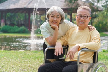 Yaşlı kadın, engelli kocasını tekerlekli sandalyede kucaklarken parkta mutluluktan dinleniyor..