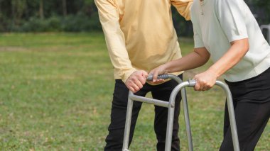 Yaşlı adam, parkta rehabilitasyon yaparken sevgili karısına Walker çerçevesiyle yürümesinde yardım ediyor..