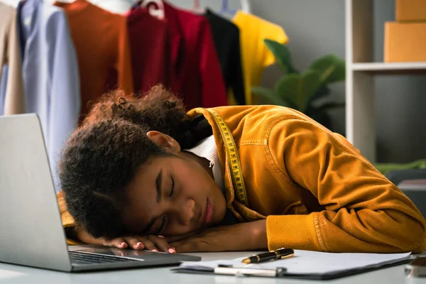African american designer woman sleeping on desk in atelier after exhausted from designing clothes.