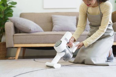 Hizmetçi oturma odasındaki tozları temizlemek için kablosuz elektrik süpürgesiyle halıyı süpürüyor..