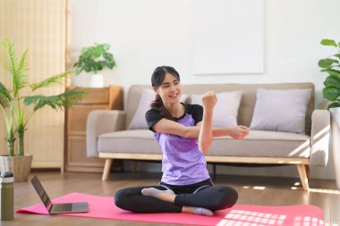 Sportif kadın yoga eğitimini internetten izliyor ve evde yoga yapmak için kollarını esnetiyor..