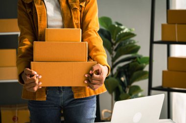 Afrika kökenli Amerikalı bir kadın, merkez büroda çalışırken müşteriye teslimat için paket kutusu taşıyor..