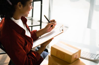 Afrikalı Amerikalı bir kadın internetten alışveriş siparişlerini kontrol ediyor ve panoya notlar yazıyor..