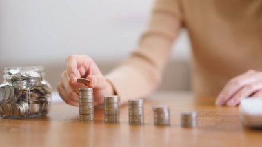 Saving money concept, Young Asian woman pick up a coin from glass jar and place it on the coin pile.