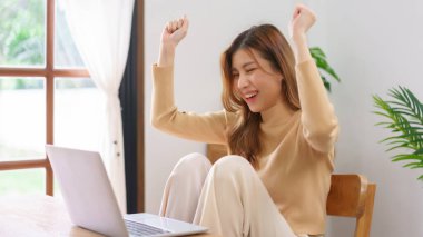 Ev kavramından çalış, genç Asyalı kadın iyi haberler aldıktan sonra kollarını kaldırsın ve başarılı bir şekilde çalışsın..