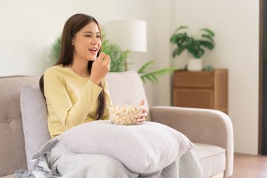 Concept of activity in home, Young woman eating popcorn while watching movie and sitting on couch.