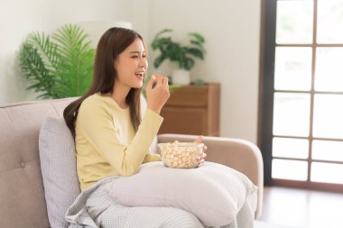 Concept of activity in home, Young woman eating popcorn while watching movie and sitting on couch.