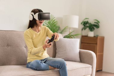 Eğlence aktiviteleri konsepti, VR gözlükleri ve joystick konsoluyla heyecan verici bir oyun oynayan genç kadın..
