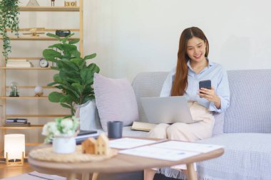 Home office concept, Businesswoman reading marketing plan data on smartphone and working on laptop.