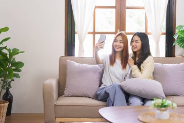 Ev kavramında rahatlayın, LGBT lezbiyen çifti gülümsüyor ve akıllı telefonu birlikte selfie çekmek için kullanıyorlar..