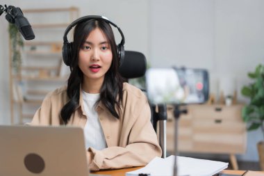 Kadın podcaster akıllı telefon kullanır ve mikrofonda izleyicilerle video podcast kaydı için konuşur.