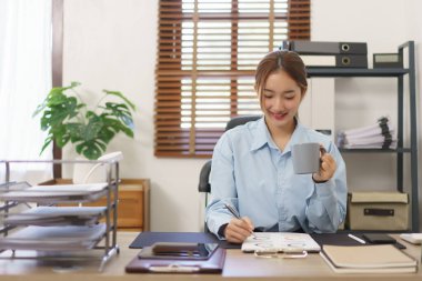 Business concept, Businesswomen is writing data in document while drinking coffee at workplace.