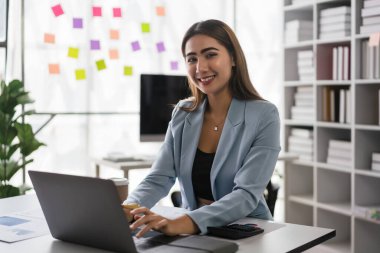 İş kadını, iş stratejisini analiz etmek ve dizüstü bilgisayarda veri yazmak için finans belgesi okuyor.