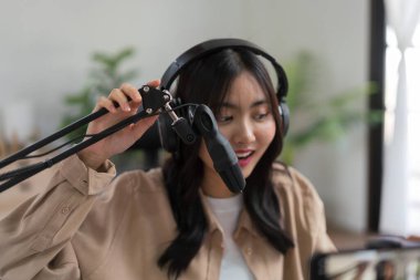 Video yayınını kaydetmek için akıllı telefon kullanan ve mikrofona haberlerden bahseden bir kadın podcaster..