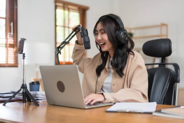 Video yayınını kaydetmek için akıllı telefon kullanan ve mikrofona haberlerden bahseden bir kadın podcaster..