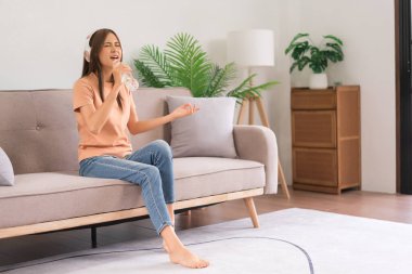 Relaxation concept, Young woman in headphone sitting on the couch and hold water bottle to singing.