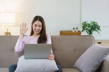 Kadınlar büyük kanepede oturuyor ve arkadaşlarıyla videoda selamlaşıyorlar. Evdeki yaşam tarzında laptoptan arıyorlar..