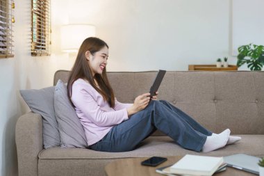 Kadınlar büyük kanepede oturup yastığa yaslanarak evdeki yaşam tarzıyla tabletten film izliyorlar..