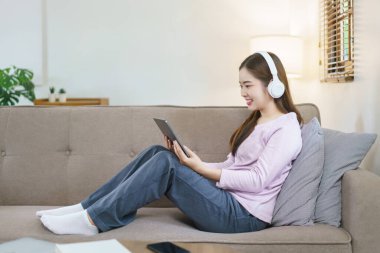 Kadınlar büyük kanepede oturuyor ve kulaklık takıyor. Evde tabletle film izliyorlar..