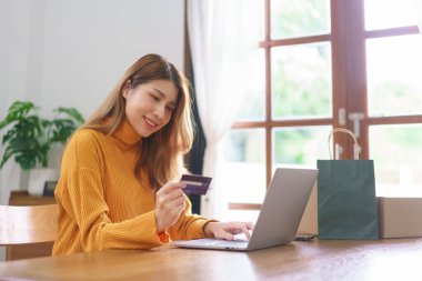 Genç Asyalı kadın internette alışveriş yapmak için dizüstü bilgisayarına kredi kartı verileri yazıyor..