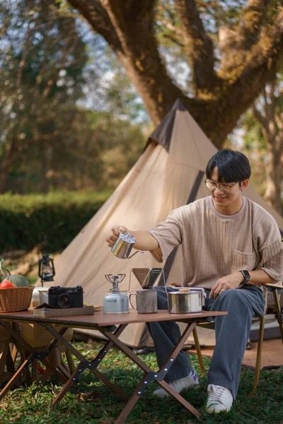 Camping concept, Man camping near lake and sits outside tent to pouring water for make coffee drip.