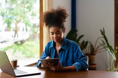 Afrikalı Amerikalı iş kadını yeni iş planlama ve tablet üzerine notlar yazma hakkında düşünüyor..