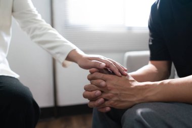 Psychologist woman touching hands to encouraging man with mental health problem in therapy center. clipart