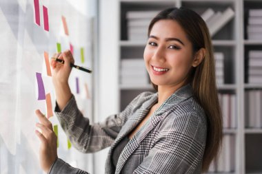 İş kadını, cam duvara yapışkan notlarla yeni iş projesiyle ilgili strateji fikirleri yazıyor..