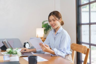 Business at home concept, Businesswoman is reading marketing data in notebook and working on laptop.