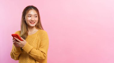Young women holding smartphone and looking outside with empty space on isolated pink background.
