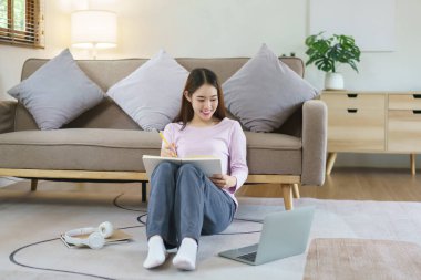 Kadınlar iş verilerini dizüstü bilgisayarda okuyor ve evde yerde otururken notlar yazıyorlar..