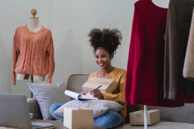 Afrikalı Amerikalı moda taciri kadın çevrimiçi sipariş yazıyor ve teslimat için paket kutusu hazırlıyor..
