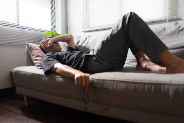 Akıl sağlığı sorunu olan bir adam kanepede yatar ve gözü depresyonlu duygularla kapatmak için kolunu kullanır..