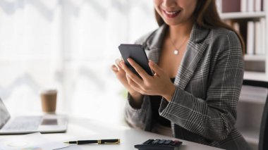 Finans belgesiyle çalışırken akıllı telefondaki iş verilerini kontrol eden iş kadını.