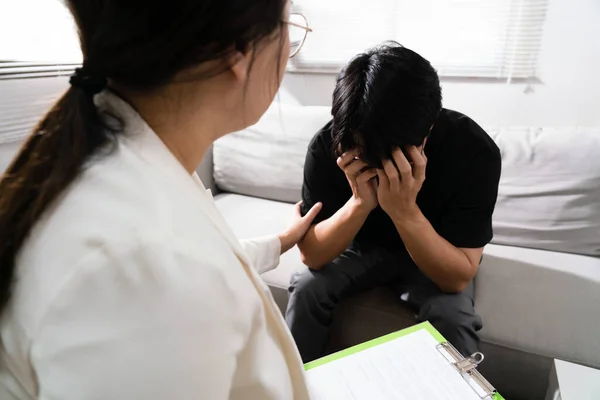 セラピーセンターで精神衛生上の問題を抱えるうつ病の男性を奨励する心理学者女性 ストックフォト