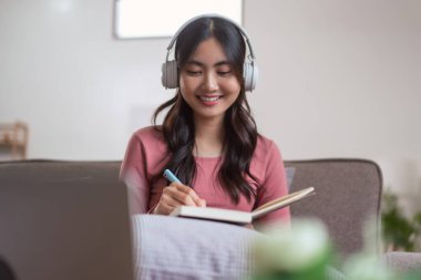 Müzik dinlerken kulaklık takan ve evdeki yaşam tarzıyla günlük defterine notlar yazan kadınlar..