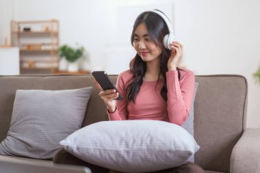 Akıllı telefondan müzik dinlemek için kulaklık takan kadınlar evdeki yaşam tarzında kanepede dinlenirken....