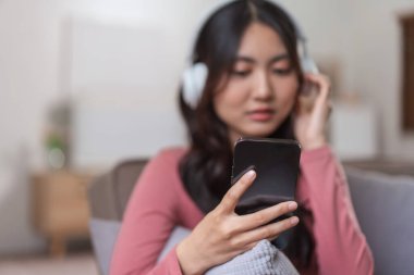Kulaklıklı kadınlar akıllı telefonlarıyla video konuşmalarında boş vakitlerinde evdeki yaşam tarzlarında kanepede oturuyorlar..
