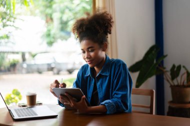 Afrikalı Amerikalı iş kadını yeni iş planlama ve tablet üzerine notlar yazma hakkında düşünüyor..