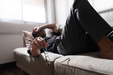 Akıl sağlığı sorunu olan bir adam kanepede yatar ve gözü depresyonlu duygularla kapatmak için kolunu kullanır..