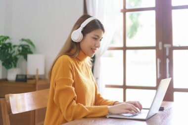 Ev konseptinde çalışmak, Asyalı bir kadının dizüstü bilgisayarda veri yazması ve kulaklık takıp müzik dinlemesi..