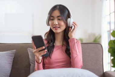 Akıllı telefondan müzik dinlemek için kulaklık takan kadınlar evdeki yaşam tarzında kanepede dinlenirken....