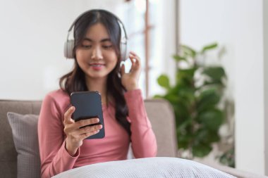 Akıllı telefondan müzik dinlemek için kulaklık takan kadınlar evdeki yaşam tarzında kanepede dinlenirken....