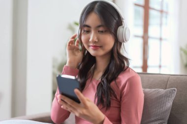 Akıllı telefondan müzik dinlemek için kulaklık takan kadınlar evdeki yaşam tarzında kanepede dinlenirken....