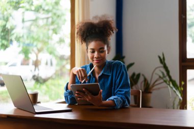 Afrikalı Amerikalı iş kadını yeni iş planlama ve tablet üzerine notlar yazma hakkında düşünüyor..
