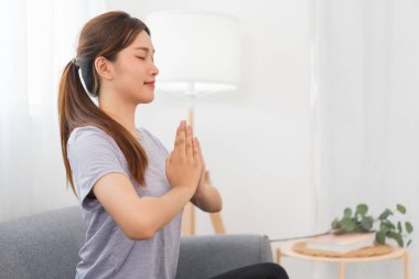 Yoga exercise concept, Young Asian woman doing yoga exercise in lotus pose with namaste on couch.