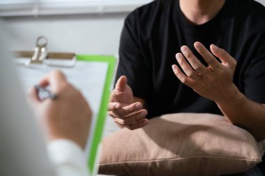 Psikolog tanısal muayene yapıyor ve erkek akıl sağlığı sorunuyla konuşurken not alıyor..