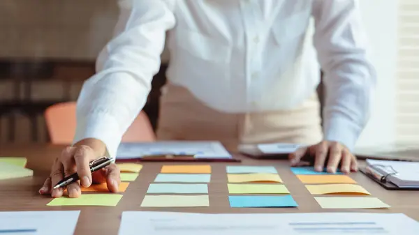 Businesswoman writing data in sticky notes on table to sharing ideas about strategy of new business.